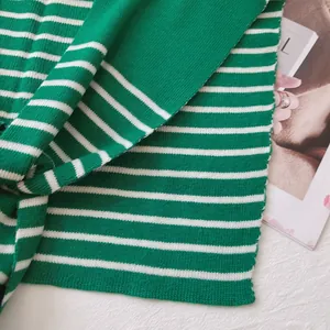 Detail shot of green and white striped knit shawl on white textured background