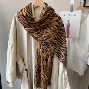 Detailed tiger print scarf with gold accents and soft tassels on beige coat
