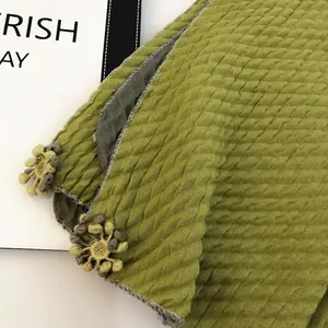 Detail of green cotton linen scarf with diamond texture and 3D knit floral pendant
