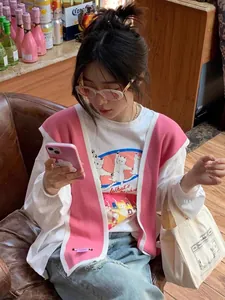 Detail of white knit vest shawl with pink trim and dancing cats graphic t-shirt