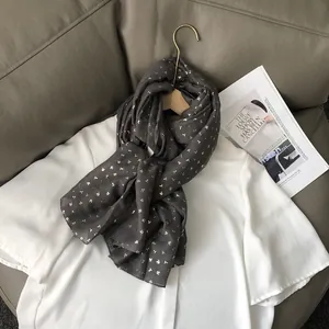 Détail d'une écharpe grise à motif trèfle doré suspendue à un crochet en bois sur chemise