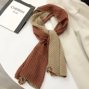 Detail of a dual-color linen scarf with diamond pleats and floral pendant accents
