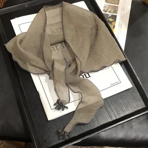 Detail of taupe chiffon shawl scarf featuring gray contrast edges and small tassel charms