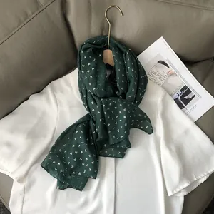 Détail d'un châle léger vert foncé avec un élégant imprimé floral doré sur un cintre