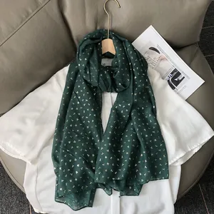 Détail de l'écharpe vert foncé avec motif feuille dorée sur une chemise blanche