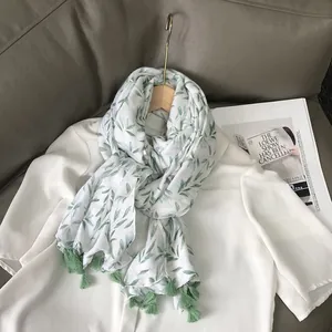Elegant white cotton linen scarf with green leaf print and tassels on a shirt