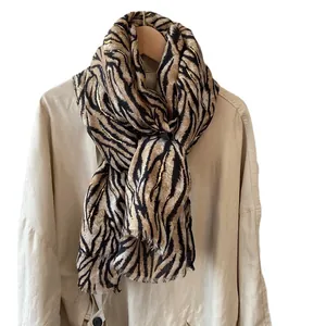 Tiger pattern scarf with gold foil accents and fringe on beige coat hanger