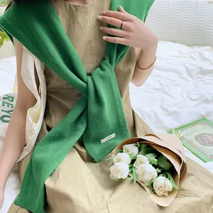 Dettaglio dello scialle in lana verde con etichetta bianca su un abito in cotone beige