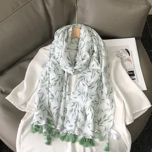 Elegant white linen feel scarf with green leaf print and tassels on a wooden hanger