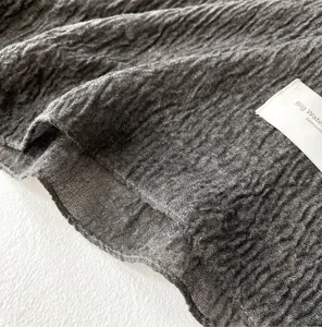 Macro detail of dark brown pleated cotton linen scarf with fine overlock stitching and label