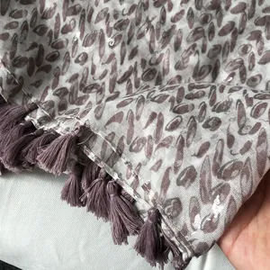 Detail of light gray scarf featuring purple grain patterns, sequins, and fringe tassels