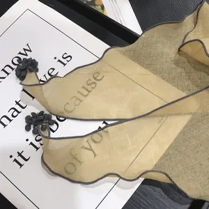 Close-up of semi-transparent scarf with wavy edges, grey pom-poms, and letter print