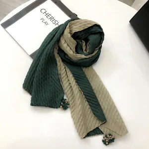Detail of bicolored linen scarf with pleated texture and decorative fringe pendant