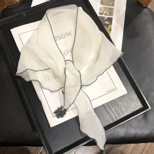 Detail of white semi-transparent scarf with dark gray edges and a black floral accent