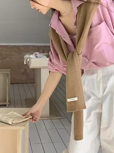 Dettaglio dell'etichetta in 100% lana australiana su camicia rosa e collana di perle