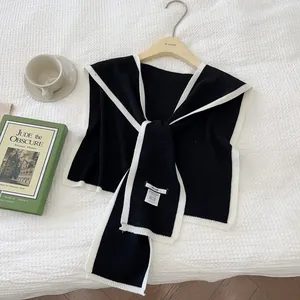 Detail of black knit shawl with white trim on wooden hanger with a cup of coffee