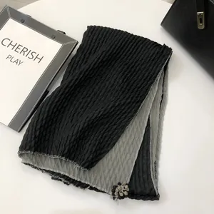 Close-up of dual-layer pleated scarf in black and grey with small pom-pom trim detail