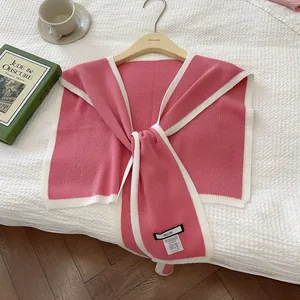 Detail of pink knit shawl showing fabric texture and woven brand label on white bedding