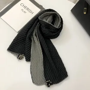 Detail of double-sided black and grey linen scarf with pleated texture and pom pom trim