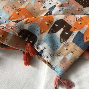 Détail d'une écharpe légère en lin avec motifs de chats et pompons orange vif