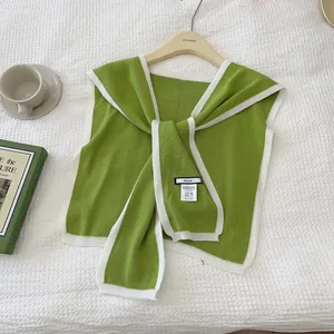 Detail of green knitted shawl with white trim featuring the brand label and soft texture