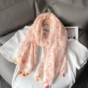 Lightweight pastel pink scarf with rainbow patterns and colorful tassels on a wooden hanger