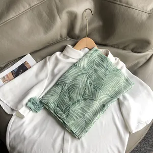 Détail de l'écharpe verte à imprimé feuilles tropicales et franges sur chemise blanche