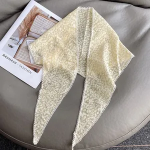 Dettaglio ravvicinato di foulard in pizzo beige con fiori e farfalle su sfondo grigio