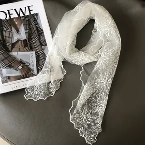 Elegant white lace scarf with floral embroidery and pearl accents on gray leather surface