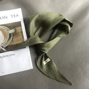 Close-up of olive green 100% linen scarf with a white tag on dark leather background