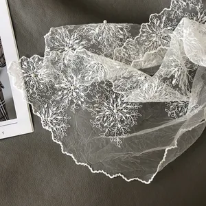 Close-up of white lace scarf with leaf embroidery and pearl accents on dark background