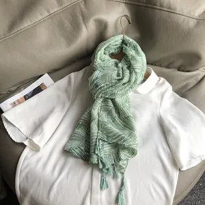 Détail d'une écharpe en mousseline vert clair avec imprimés palmiers et glands élégants