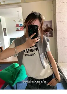 Detalle de un chal de punto de lana gris claro sobre una camiseta blanca con eslogan