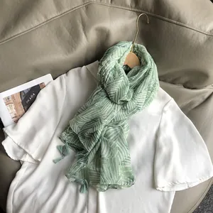 Détail d'une écharpe à imprimé feuilles vertes avec glands élégants en mousseline