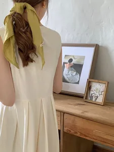 Close-up of mustard yellow silk scarf tied on ponytail with pleated cream dress detail