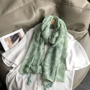 Détail de l'écharpe vert clair à imprimé feuilles de palmier et pompons élégants