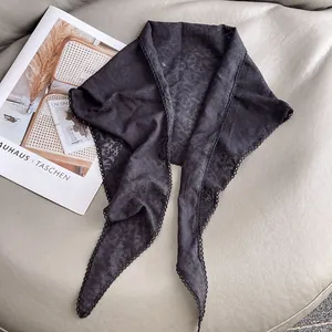 Dettaglio di un foulard triangolare in pizzo nero con ricami floreali e bordo all'uncinetto