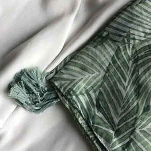 Détail du châle aux feuilles tropicales vertes avec pompons sur tissu blanc doux