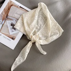 Dettaglio del foulard a triangolo in pizzo beige con ricami floreali e bordi a smerlo