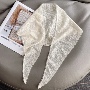 Dettaglio del foulard in pizzo beige con ricami floreali e bordi a conchiglia