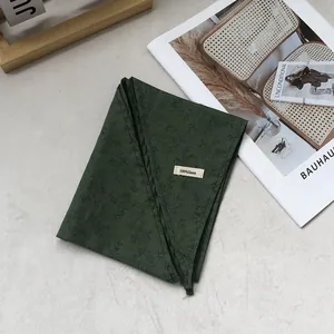 Close-up of dark green linen scarf fabric with leaf pattern and 100% linen label