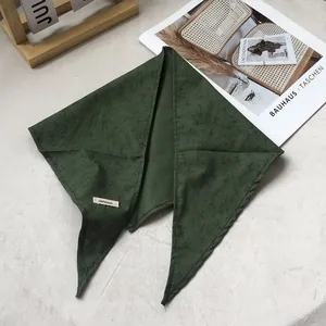 Detail of dark green 100% linen triangle scarf with leaf pattern on soft background