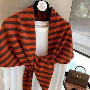 Detalle de bufanda triangular de lana a rayas colocada sobre un jersey blanco suave