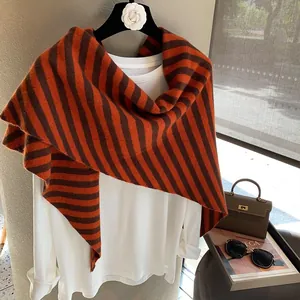 Detalle de bufanda triangular de lana a rayas combinada con una blusa blanca fina