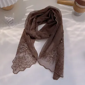 Detail of brown lace scarf with floral embroidery and white pearl beads on wavy edges