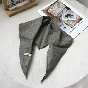 Close-up of dark green linen triangle scarf showing 100% linen label and floral print