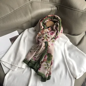 Écharpe en coton et lin à fleurs roses avec bordure verte sur un haut blanc