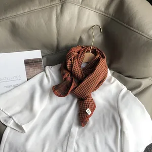 Close-up of a brown plaid cotton neck scarf draped over a white shirt on a wooden hanger