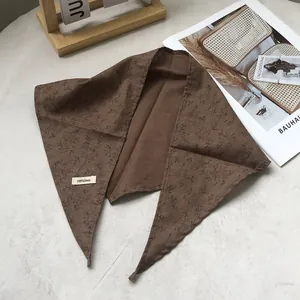 Close-up of brown linen triangle scarf with leaf pattern and 100% linen fabric label