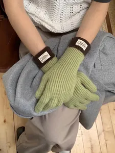 Detail of green knitted gloves with brown ribbed cuffs and a white branded label